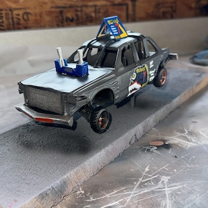 May include: A gray die-cast toy car featuring a blue roof sign with the text Octane, a blue engine intake with two silver pipes on the hood, and a graphic on the side door depicting a shark mouth with teeth and the text Octane in yellow and blue.