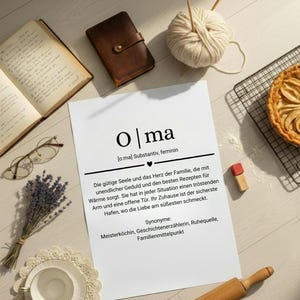 Könnte beinhalten: Ein Stillleben mit einem weißen Papier mit dem deutschen Wort "Olma" und seiner Definition, umgeben von einem ledergebundenen Notizbuch, Garn, Stricknadeln, einem Kuchen und einer Tasse Tee.