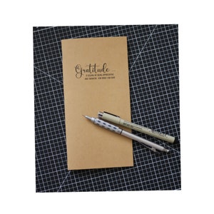 May include: A brown notebook with the text "Gratitude... A feeling of being appreciative and thankful for what you have." written in black cursive.
