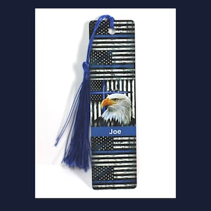 May include: A blue and white personalized bookmark with a thin blue line American flag design, a bald eagle, and the word "Faith" with a cross. The bookmark has a blue tassel and the name "Joe" is printed on the bookmark.