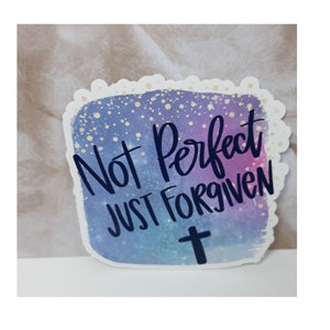 May include: A sticker with a watercolor background in shades of blue, purple, and pink with gold glitter. The sticker has the text "Not Perfect Just Forgiven" in black lettering and a black cross.