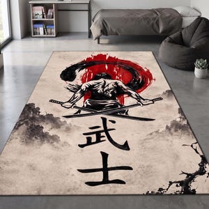May include: A rectangular area rug featuring a central illustration of a warrior seen from behind, holding two crossed swords. The design includes a large red circular sun motif, black ink-style brush strokes, and the Japanese kanji characters 武士.