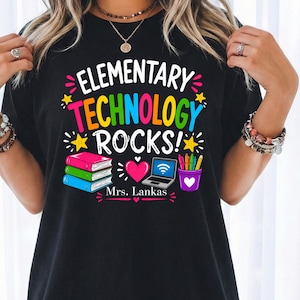 May include: A black t-shirt featuring a colourful graphic with the text "ELEMENTARY TECHNOLOGY ROCKS!" and "Mrs. Lankas". The design includes a stack of three books, a pink heart, a laptop with a Wi-Fi symbol, and a purple cup filled with coloured pencils.
