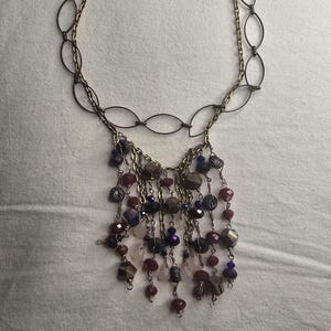 May include: A necklace with a two-tone chain and a cascade of beads. The upper chain is made of oval links, while the lower chain is a finer gold color. The beaded section features a mix of red, purple, and iridescent beads.