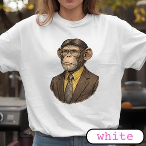 Op de afbeelding: Wit T-shirt met een gedetailleerde illustratie van een chimpansee met een bril, een geel overhemd, een stropdas met patroon en een bruin jasje. Het woord "white" staat in een wit afgerond rechthoekje onderaan de afbeelding.