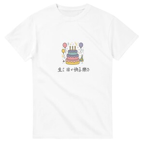 May include: White t-shirt featuring a colorful illustration of a birthday cake with candles, balloons, and confetti. The cake has multiple layers in shades of pink, purple, and yellow. The text "Happy Birthday" is written in Japanese below the cake.