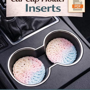 May include: Crochet car cup holder inserts in a car's console. The inserts are circular, with a gradient of pink, white, and blue yarn. The image includes text that reads "Crochet Pattern PDF Car Cup Holder Inserts."