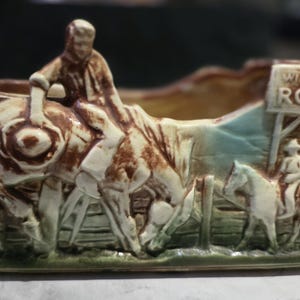 May include: A rectangular ceramic planter with a Wild West rodeo theme. The planter features a relief sculpture of a cowboy riding a bucking bronco, with other cowboys and horses. The words "Wild West Rodeo" are visible.