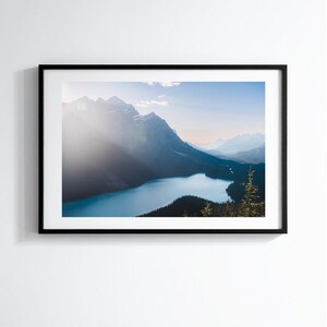 Peut inclure: Photographie encadrée d'un paysage avec un lac serein entouré de montagnes sous un ciel clair. L'eau est d'un bleu profond, reflétant le ciel et les sommets environnants. La photographie est dans un cadre noir.