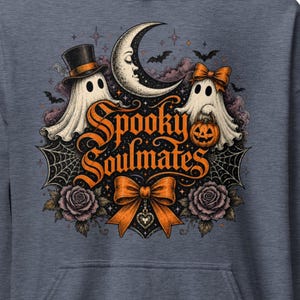 Pode incluir: Um capuz azul-escuro mesclado com uma estampa gráfica de dois fantasmas, um usando cartola e o outro um laço, com uma lua crescente, morcegos, teias de aranha, rosas e um laço laranja com o texto Spooky Soulmates impresso no centro.
