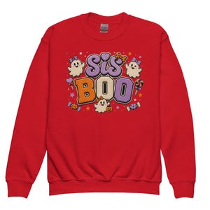 May include: A red crew neck sweatshirt featuring the text "Sis Boo" in orange and purple, with ghost and candy illustrations. Ideal for Halloween, this sweatshirt is a cosy autumn garment.
