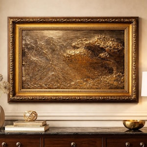 Könnte beinhalten: Ein gerahmtes Kunstwerk in Gold- und Brauntönen. Das Gemälde zeigt eine strukturierte, abstrakte Landschaft. Es wird über einer dunklen Holzkommode mit einer Lampe und dekorativen Gegenständen ausgestellt.