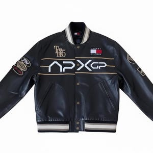 May include: Black leather varsity jacket with white and gold accents. Features the text "TH 185" and "APX GP" along with Tommy Hilfiger branding. Includes patches on the sleeves and striped cuffs and collar.