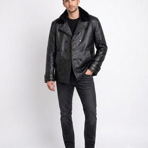 Könnte beinhalten: Eine zweireihige schwarze Lederjacke mit schwarzem Kunstfellkragen, langen Ärmeln mit Schnallenmanschetten und Knopfverschluss. Die Jacke wird mit einer dunkelgrauen Jeans und schwarzen Ledersneakern über einem schwarzen T-Shirt kombiniert.