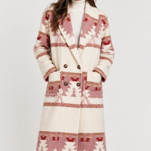 May include: A long, double-breasted coat in cream, featuring a geometric pattern in shades of dusty rose, muted red, and tan. The coat has a wide lapel, two front patch pockets, and four dark brown buttons, worn over a white ribbed turtleneck.