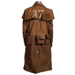 May include: A brown long coat featuring a wide shoulder yoke with the text A7 printed in a light, weathered font. The garment includes three distinct rectangular pockets with button closures across the waist area and a central back vent.
