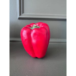 May include: A bright red bell pepper with a smooth, glossy surface and a distinct lobed shape. The top features a small, light green stem area nestled within the central depression, showcasing a realistic appearance and vibrant color saturation.