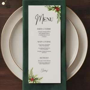Puede incluir: Una tarjeta de menú festiva con la palabra "MENU" en escritura elegante. La tarjeta presenta un diseño floral verde y rojo y enumera una comida de tres platos. El menú se coloca en un plato blanco con borde dorado, una servilleta verde y cubiertos dorados.