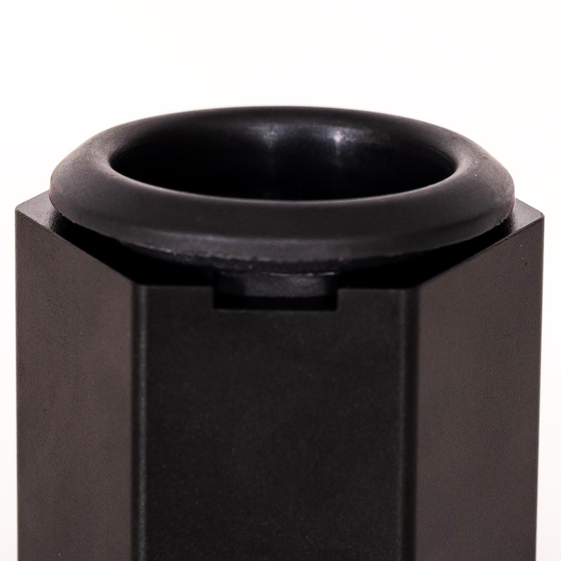 May include: A matte black hexagonal object featuring a circular opening at the top. The top edge is finished with a smooth, rounded black rim that sits flush against the flat, angled sides of the hexagonal structure, creating a clean profile.