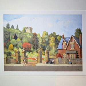 May include: A framed watercolor painting depicts a scenic landscape with a red brick house, a stone gate, and a castle on a hill. The artwork features lush trees in various colors, a blue sky, and people walking in the distance.