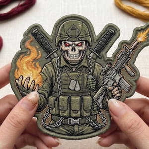 Puede incluir: Un parche bordado detallado que muestra a un soldado esqueleto con uniforme táctico y casco verdes. La figura sostiene una mano en llamas y un rifle con fogonazo, con dos espadas cruzadas detrás y placas de identificación al cuello.