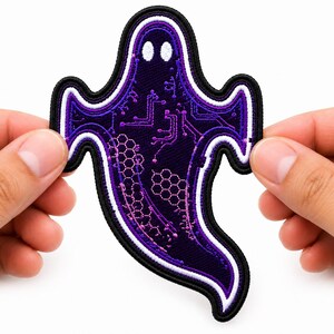 May include: An embroidered ghost-shaped patch featuring a dark purple base with a light purple circuit board pattern and a honeycomb design. The patch has two white oval eyes and is outlined with thick black, white, and purple stitched borders.