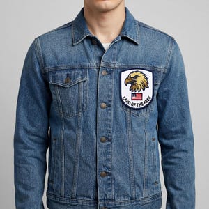 May include: A blue denim jacket with a patch featuring a golden eagle head and the text "LAND OF THE FREE" with a small American flag. The patch is rectangular with a white border.