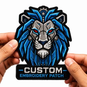 May include: An embroidered patch featuring a stylized mechanical lion head with a silver face, bright red eyes, and a vibrant blue mane. Below the lion, a black rectangular base displays the white text CUSTOM and blue text EMBROIDERY PATCH.