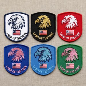 May include: Six embroidered patches with an eagle design and the text "LAND OF THE FREE". The patches are in various colors, including white, black, red, blue, and green, with the eagle in different colors as well. Each patch features a small American flag.