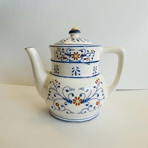 May include: A white ceramic mug with a black handle and the text "But First, Coffee" in a bold, black font. The mug is set against a blurred background, suggesting a cozy setting.