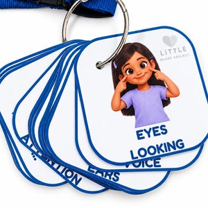 May include: A set of square educational flashcards on a metal ring with a blue lanyard. Each white card features a blue border and a cartoon illustration of a person pointing to body parts or actions with text labels including EYES, LOOKING, VOICE, EARS, and ATTENTION. The Little Minds Project logo is printed on the top right corner of the cards.