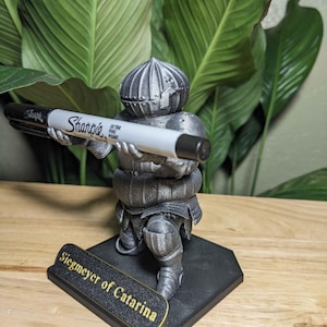May include: A 3D-printed figurine of a knight holding a Sharpie marker. The knight is silver and black, with the text "Siegmeyer of Catarina" on the base. The Sharpie is black and white.