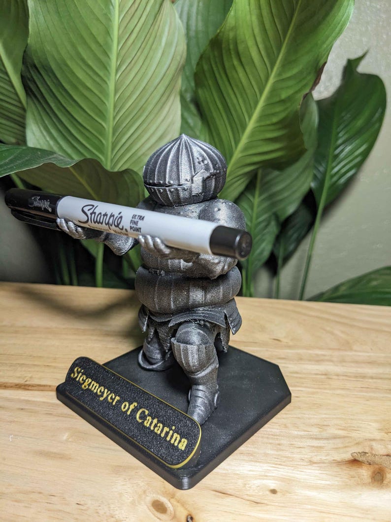 May include: A 3D-printed figurine of a knight holding a Sharpie marker. The knight is silver and black, with the text "Siegmeyer of Catarina" on the base. The Sharpie is black and white.