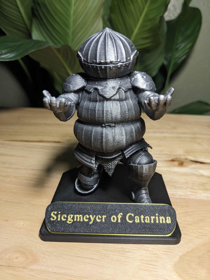 May include: A detailed, gray figurine of a knight in armor, with the text "Siegmeyer of Catarina" on a base. The knight has a round helmet, shoulder pads, and a segmented torso. The figurine is posed with arms outstretched.
