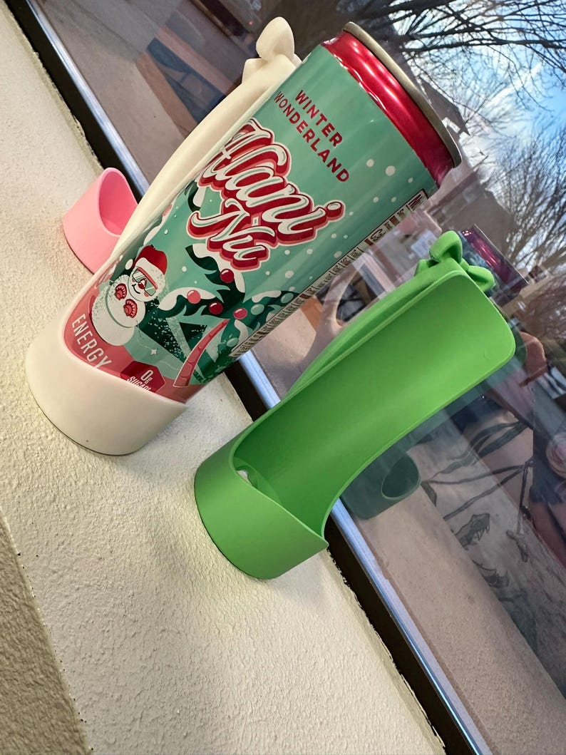 May include: A can of "Winter Wonderland" energy drink in a white and green holder, with a pink and green holder nearby. The can has a red top and features a snowman graphic. The text "Winter Wonderland" and "Hans Ne" are visible.