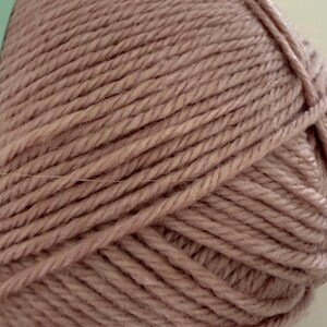 Puede incluir: Primer plano de una madeja de hilo rosa empolvado. El hilo est&aacute; bien enrollado, mostrando hebras individuales con una apariencia texturizada. El color es un rosa-marr&oacute;n apagado, adecuado para proyectos de tejido o ganchillo.