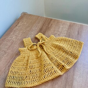 May include: Mustard yellow crochet shorts with a tie at the waist. The shorts are handmade with a textured stitch pattern. The garment is displayed on a wooden surface.