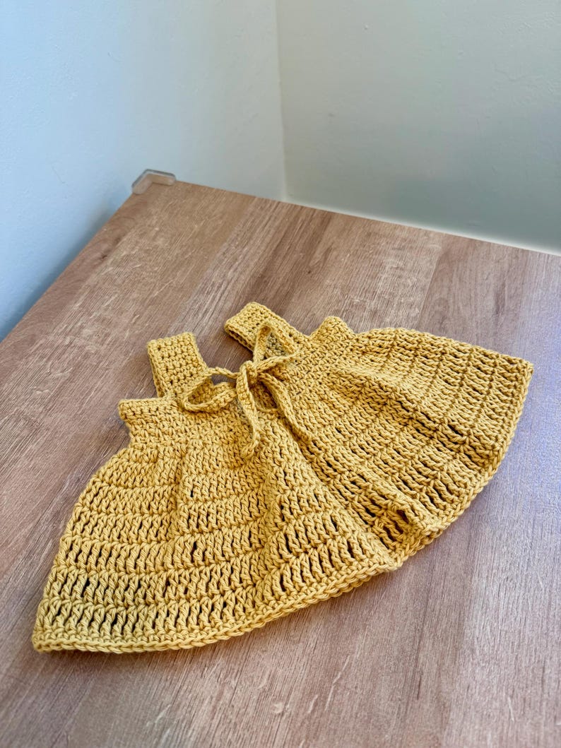 May include: Mustard yellow crochet shorts with a tie at the waist. The shorts are handmade with a textured stitch pattern. The garment is displayed on a wooden surface.