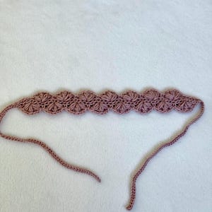Pu&ograve; includere: Una fascia per capelli all'uncinetto color malva con un design a conchiglia. La fascia presenta una serie di motivi a forma di fiore collegati lungo la parte anteriore. Le estremit&agrave; della fascia sono lunghe, sottili e senza decorazioni, che consentono di legarla.