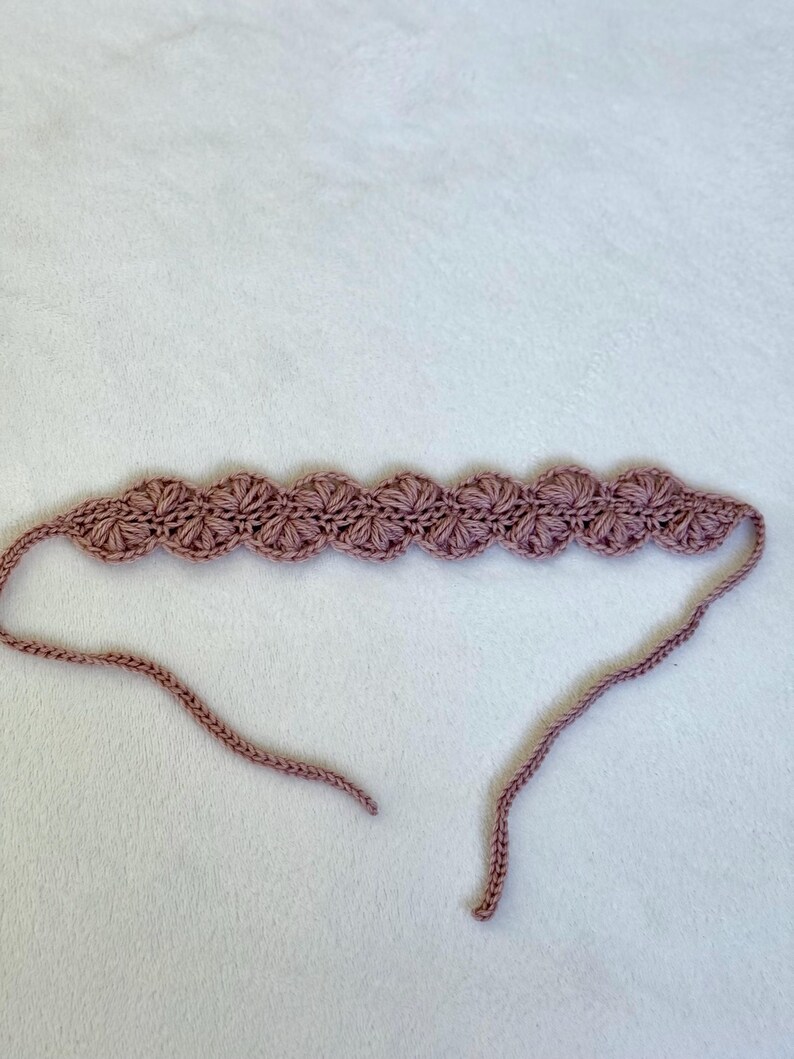 Pu&ograve; includere: Una fascia per capelli all'uncinetto color malva con un design a conchiglia. La fascia presenta una serie di motivi a forma di fiore collegati lungo la parte anteriore. Le estremit&agrave; della fascia sono lunghe, sottili e senza decorazioni, che consentono di legarla.