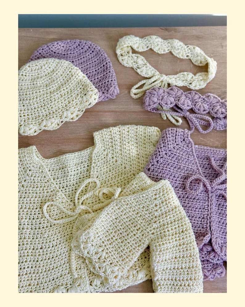 K&ouml;nnte beinhalten: Eine Sammlung handgefertigter H&auml;kelartikel, bestehend aus zwei Strickjacken, zwei M&uuml;tzen und zwei Stirnb&auml;ndern in Creme- und Lavendelt&ouml;nen. Die Strickjacken haben Bindeb&auml;nder, w&auml;hrend die M&uuml;tzen und Stirnb&auml;nder mit Bogenkanten versehen sind.