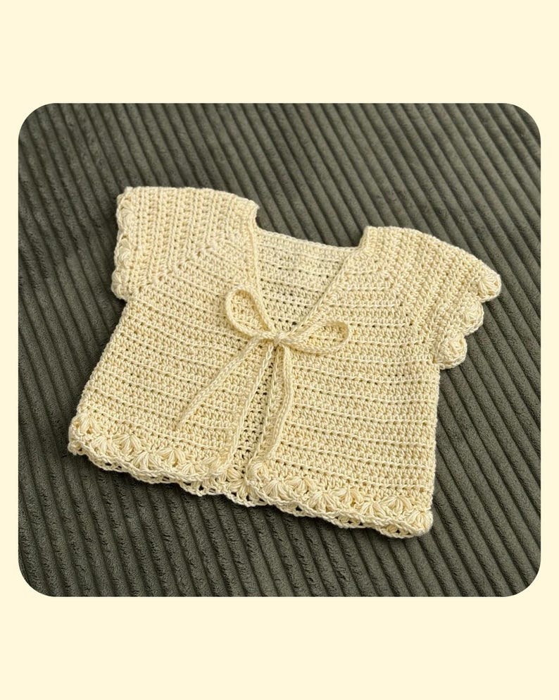 Pu&ograve; includere: Un cardigan all'uncinetto color giallo pallido con maniche corte dai bordi smerlati, scollo rotondo e chiusura frontale a fiocco realizzata con lo stesso filato. Il capo presenta un motivo a punti costante e un bordo decorativo.