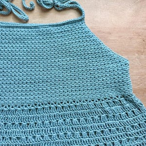 Pu&ograve; includere: Un top all'americana all'uncinetto color azzurro caratterizzato da un motivo a maglia denso e uniforme nella parte superiore e da un motivo decorativo in pizzo traforato sull'orlo svasato, con lacci all'uncinetto abbinati al collo e sulla schiena.