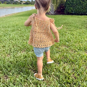 May include: A sleeveless crochet top in a speckled golden-yellow yarn featuring tie-shoulder straps and a decorative open-stitch pattern at the hem, paired with light blue denim shorts and mustard-colored canvas sneakers with white rubber soles.