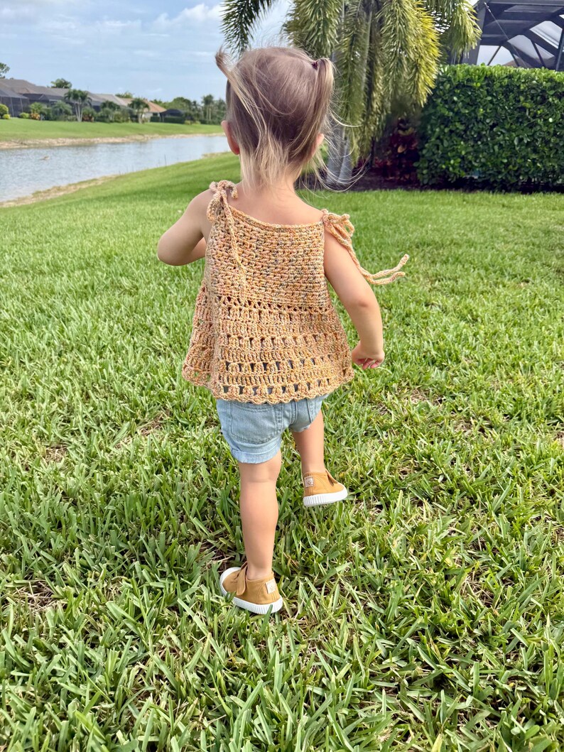 May include: A sleeveless crochet top in a speckled golden-yellow yarn featuring tie-shoulder straps and a decorative open-stitch pattern at the hem, paired with light blue denim shorts and mustard-colored canvas sneakers with white rubber soles.