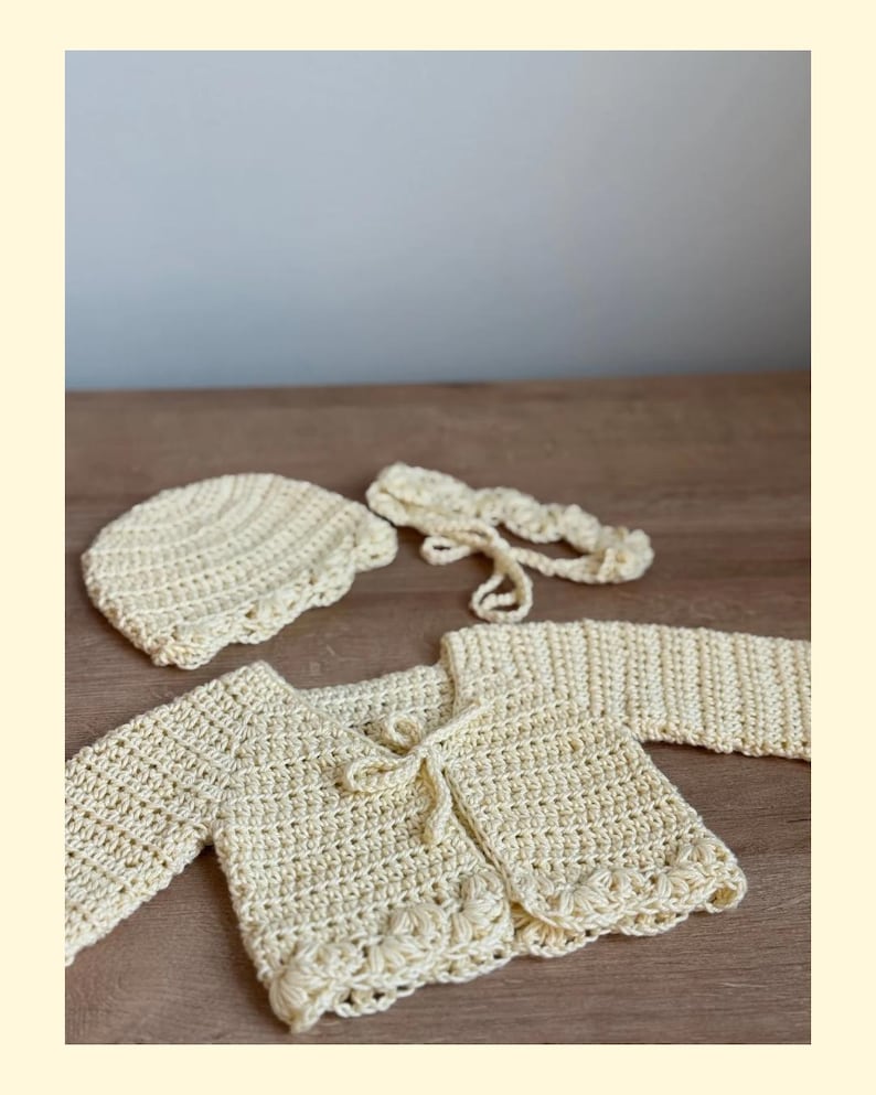 K&ouml;nnte beinhalten: Ein hellgelbes H&auml;kelset bestehend aus einer lang&auml;rmeligen Strickjacke mit Bindeband vorne und dekorativem Wellensaum, einer passenden runden Haube mit strukturiertem Muster sowie einem d&uuml;nnen, geflochtenen Stirnband mit Bindeb&auml;ndern.