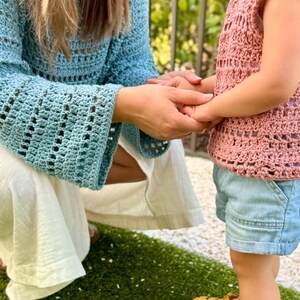 Op de afbeelding: Een lichtblauw gehaakt shirt met lange mouwen en een grof breipatroon, gecombineerd met een witte broek. Een mouwloos oudroze gehaakt shirt met een bijpassend grof patroon, lichtblauwe spijkerbroek en mosterdgele rubberen sandalen met gespen.