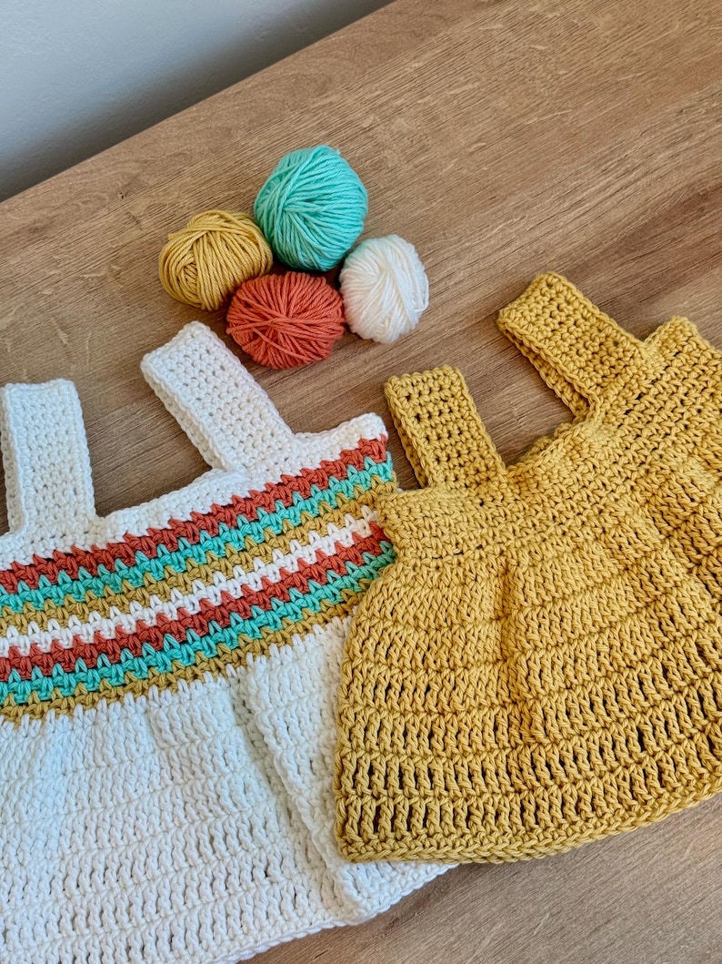 May include: Two crochet tops, one white with a colorful striped design and one yellow, are displayed with several balls of yarn in shades of yellow, orange, teal, and white. The tops have strap details and are handmade.