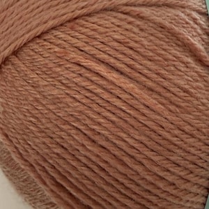 Puede incluir: Primer plano de una madeja de hilo en un tono c&aacute;lido y terroso. El hilo tiene un aspecto texturizado, con hebras visibles y una superficie ligeramente irregular. El color es un rosa apagado y polvoriento, adecuado para varios proyectos de tejido o ganchillo.