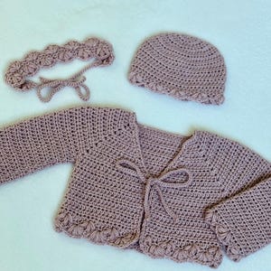 Pu&ograve; includere: Un set per neonati all'uncinetto fatto a mano, color malva, composto da un cardigan, un cappellino e una fascia. Il cardigan ha maniche lunghe e chiusura con fiocco. Il cappellino e la fascia presentano un bordo smerlato. Il set &egrave; realizzato in filato morbido.